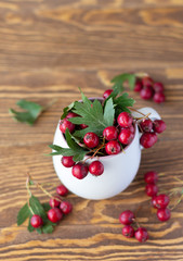 Hawthorn berries in white mug on wooden table.  Plant to make medicine for digestive and heart systems. Copy space