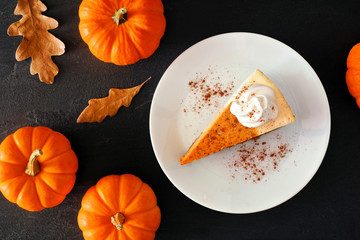 Slice of pumpkin cheesecake with whipped cream, overhead table scene with a black stone background