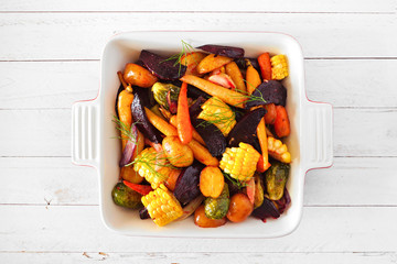 Roasted autumn vegetables in a baking dish, top view over a white wood background