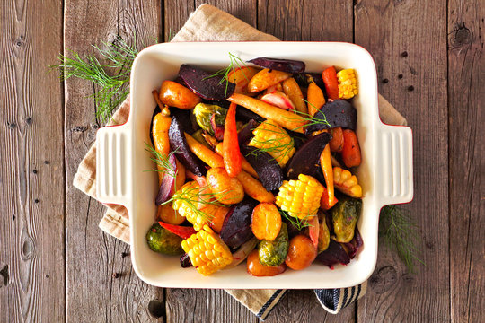 Roasted autumn vegetables in a baking dish, top view over a rustic wood background
