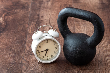 Black iron kettlebell on a rustic wood floor, with white analog alarm clock