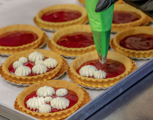Tarts with raspberry filling and cream. Decoration of tarts with cream.