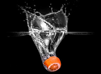 Water Splash Photography: an orange fruit falling in water creating a large splash, on a black background