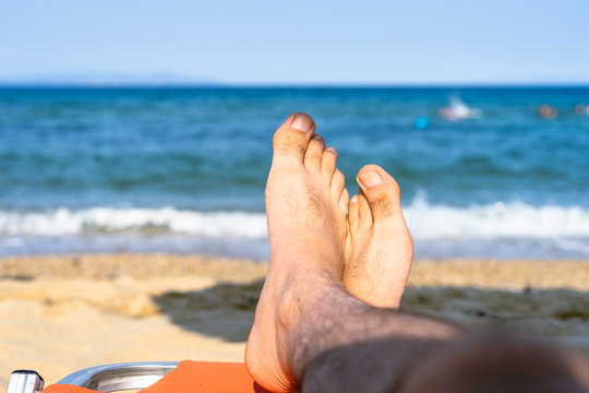 Feet foot of a man male at the beach by the sea in sunny day relaxing on vacation seaside by the ocean