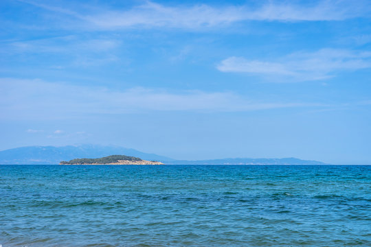 Seaside view horizon of the ocean water with an kafkanas island on the horizon in sunny day from the beach at Olympiada Greece