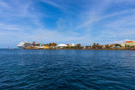 Beautiful view of coast line of Willemstad. Dark blue water surface of Atlantic ocean. Coast line with buildings and big cruise boat merging with blue sky and white clouds. Willemstad. Curasao