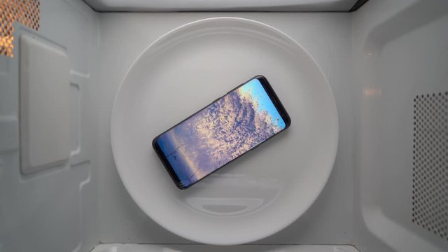 Cell phone on a plate rotating in microwave top view. Food blog concept.