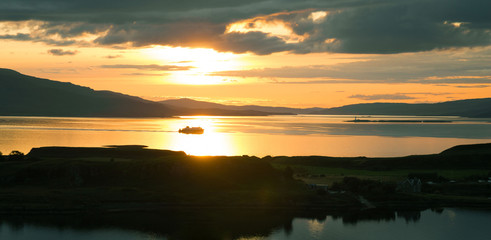 Sunset over sea from Pulpit Hill, Oban. West coast of Scotland. Isle of Kerrera in foreground and ferry sailing from Isle of Mull backlit in background. Argyll and Bute. UK. Landscape. Seascape