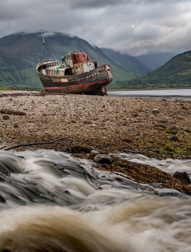 Vertical landscape. Corpach shipwreck. Old fishing boat beached near Fort William. Highlands of Scotland. Long exposure water in foreground. Clouds above Ben Nevis in background. Scotland. UK