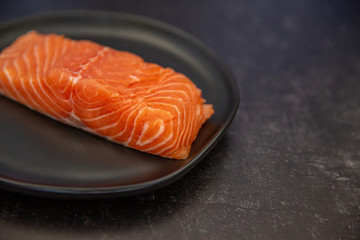 a slice piece portion of raw salmon on a black plate on a black slate surface