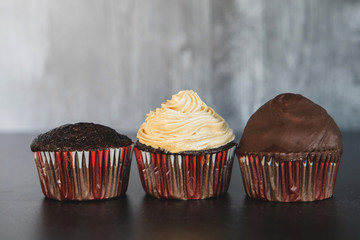 Three chocolate gourmet cupcakes. Dessert with lots of calories. One is plain with no frosting, one has peanut butter whipped frosting and the third has the peanut butter frosting dipped in chocolate