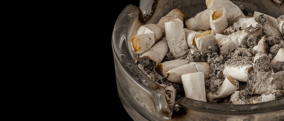 Filled glass ashtray with extinguished cigarettes, isolated on black. Copy space for text.