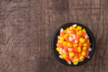 Black ceramic cauldron filled with holiday candy corn on a rustic wood background