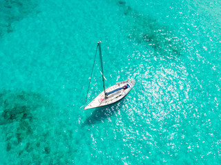 High angle aerial drone bird's eye view of a sailing yacht with sails lowered anchored in shallow,...