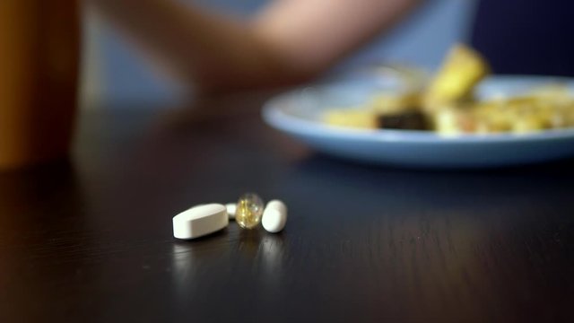Close up of pills on a table in the kitchen. on a blurred background, someone is eating food from a plate