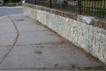 Old weathered retaining wall topped with wrought iron fencing beside a sidewalk, horizontal aspect