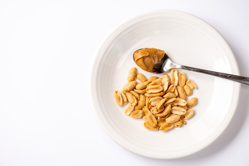 A top down view of a white plate on a white background holding peanuts and a spoonful of peanut butter with space for copy.
