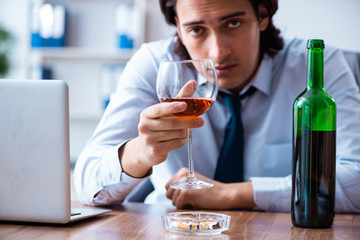 Male employee drinking alcohol and smoking cigarettes at workpla