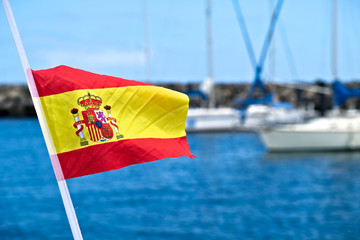 Spanish flag in the wind with sailing boats in a marina in a blurred background.