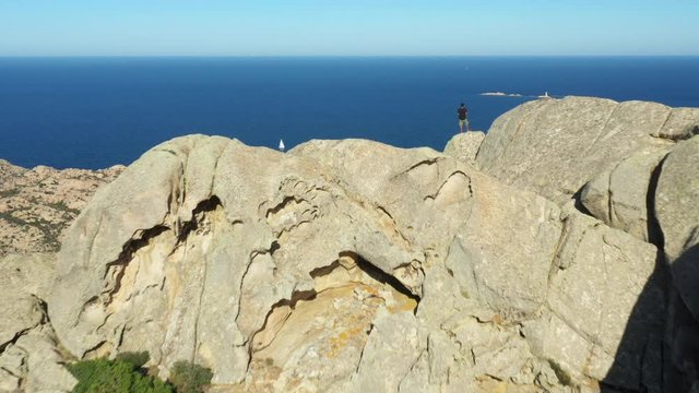 View from above, stunning aerial view of a person on the top of a granite mountain. Cala Coticcio also known as Tahiti in the background. La Maddalena Archipelago, Sardinia, Italy.