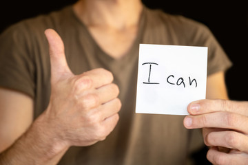 A man holds in his outstretched hand a sheet with the inscription "I can" and shows the sign of like