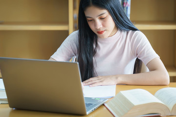 Young Asian woman student study and take notes with book in library.