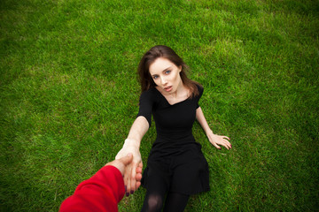 Top view portrait of a young beautiful woman in black dress lies on green lawn in a park