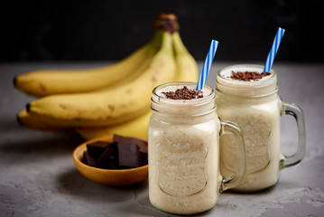 Banana milkshake in a glass with chocolate on grey concrete surface, closeup