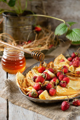Traditional Ukrainian or Russian pancakes with strawberry berries and honey on wooden table. Shrovetide Maslenitsa Butter week festival meal. Slavic cuisine concept. Beautiful drop of honey