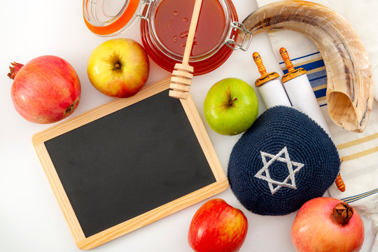 Happy Rosh Hashanah and Yom Kippur conceptual idea with shofar (ram horn), apple, pomegranate, honey, torah scroll (the holly book of judaism) and tallit (prayer shawl) with copy space on chalkboard - Powered by Adobe
