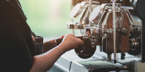 Young professional female barista making coffee with coffee maker machine