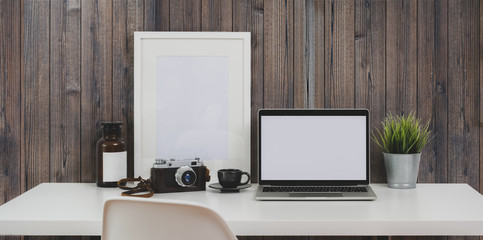 Laptop computer and mock up frame in minimal workplace with wooden rustic wall