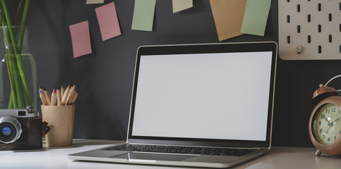 Open blank screen laptop with office supplies in dark trendy photographer workplace