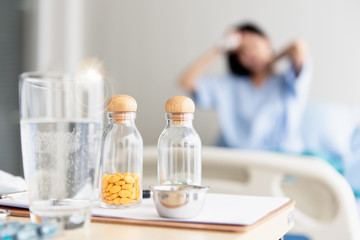 The girl sitting in the hospital's bed. She had a headache and had an illness. have medicine, a glass of water at the table. Selective focus on medicine. Achoo, flu season.