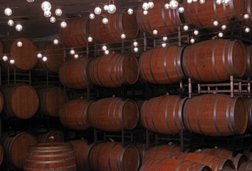 A chain of light bulbs illuminating a warehouse room with stacks of wooden wine barrels