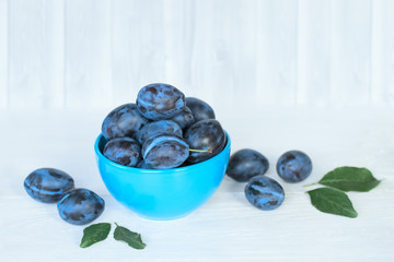 ripe blue plums with leaves in a blue bowl closeup. background with ripe fresh plums with leaves.