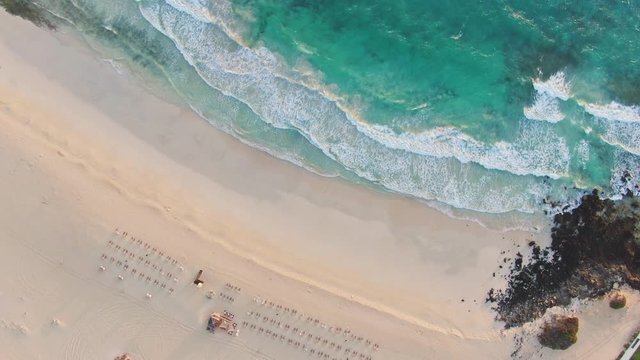 Aerial 4k panoramic bird's eye drone sunrise view of a beach section at Corralejo Natural Park (Parque Natural de Corralejo) on Fuerteventura, Canary Islands, Spain. Big waves & sunbeds for tourists.