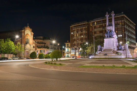 Italian city at night, art and culture. Gallarate, square Risorgimento with monument to the fallen for the homeland of the war of 1915 – 1918 (first and second world war) and church of San Francesco