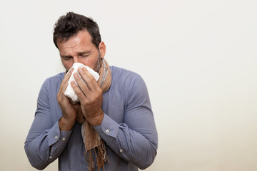 cold man dressed in shirt and scarf blowing his nose with a tissue.