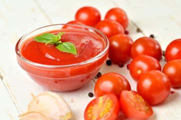 Close-up of bowl of homemade ketchup made from fresh tomatoes, garlic, basil on white rustic wooden background.