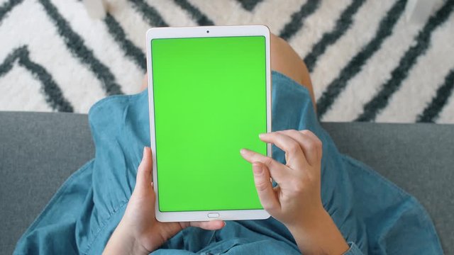 Woman uses tablet with green screen for watching video, shopping online and texting in social networks. 4k slow motion footage.  Top view.