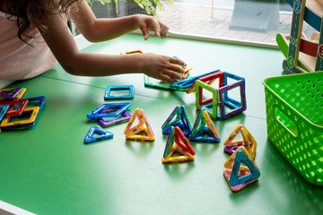 Girl in pink dress playing with magnetic geometric shape toy, hands show, no face.