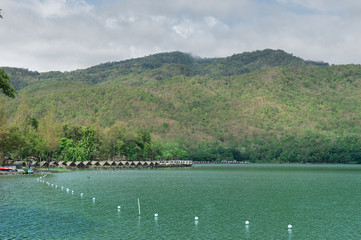 View of green lake with  small hut nearby and mountain background with big tree brunch as foreground, Vacation time in holiday concept.