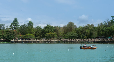 View of green lake with  small hut nearby and mountain background with big tree brunch as foreground, Vacation time in holiday concept.