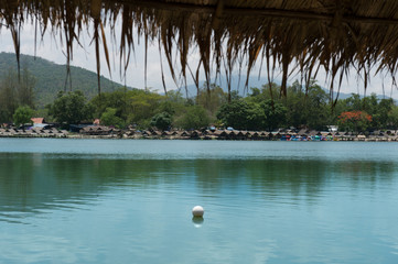 View of green lake with  small hut nearby and mountain background with big tree brunch as foreground, Vacation time in holiday concept.