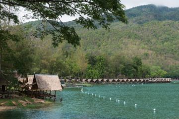 View of green lake with  small hut nearby and mountain background with big tree brunch as foreground, Vacation time in holiday concept.