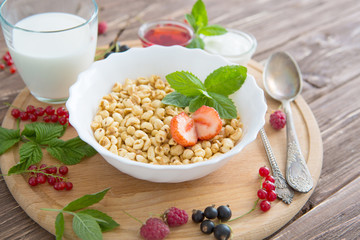 Healthy breakfast with corn flakes, berries, waffle and milk on blue background. Close up. Healthy tasty breakfast of muesli with strawberries, raspberries, black currants and red currants.