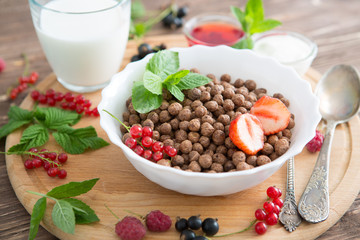 Cereal chocolate balls in bowl with milk on rustic wooden table Healthy tasty breakfast chocolate balls with strawberries, raspberries, black currants and red currants.