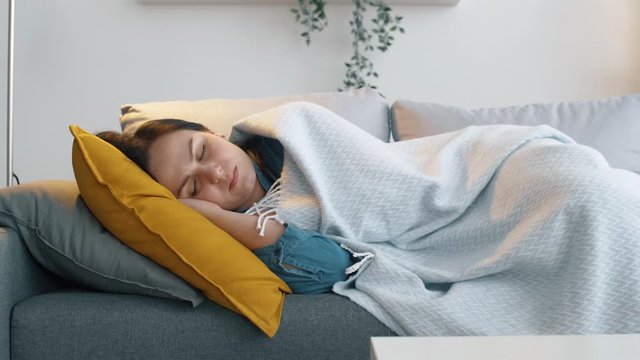 Woman sleep at home in sofa after hard work. Relax and sleeping girl with plead. Cozy atmosphere. 4k footage.