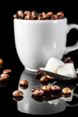 Full cup of coffee beans and spoon with sugar cubes on black.